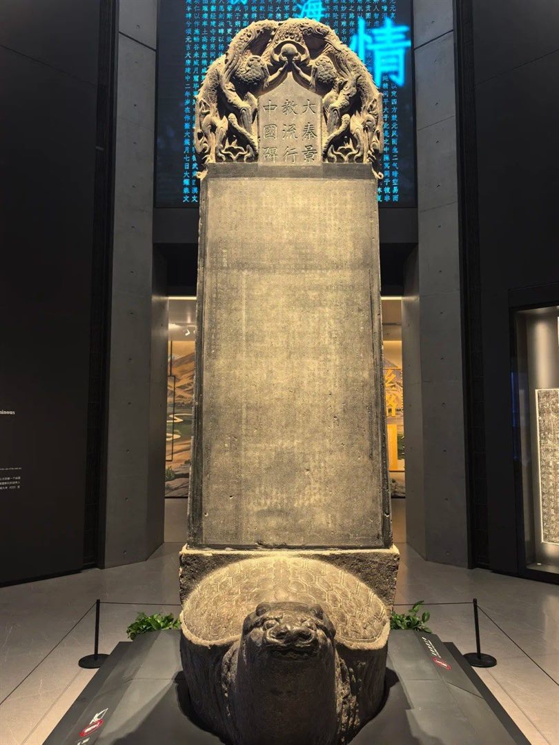 The Nestorian Stele head-on without glass, its dragon-entwined crown carrying the incised title 大秦景教流行中國碑, standing on a stone tortoise base.