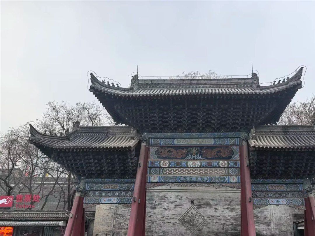 A painted triple-eave gateway in the entrance courtyard with a carved screen wall behind, and a red 售票处 Tickets sign at the far left.
