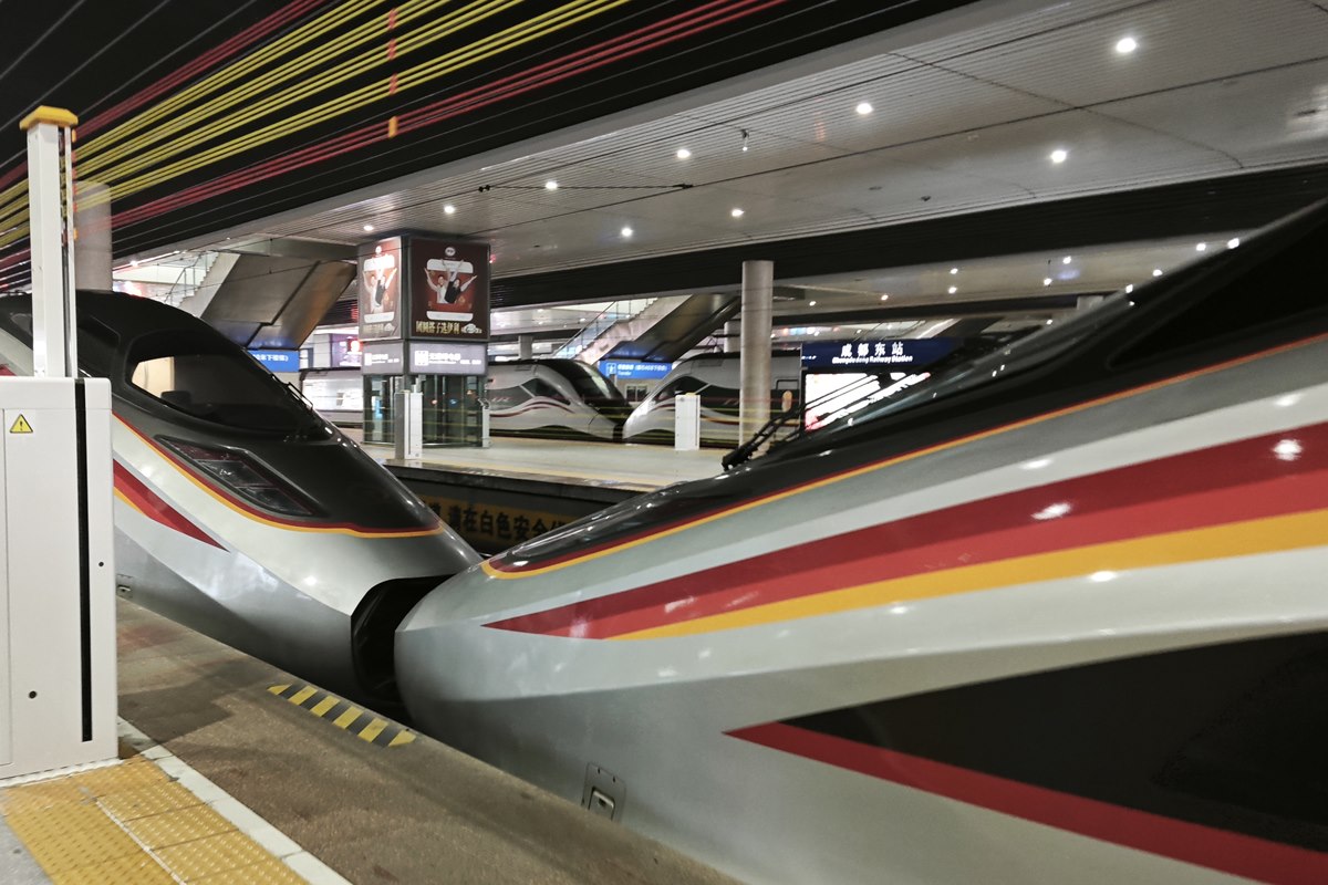 Two Fuxing high-speed trainsets nose to nose on a platform at Chengdu East, with the station name sign visible behind.