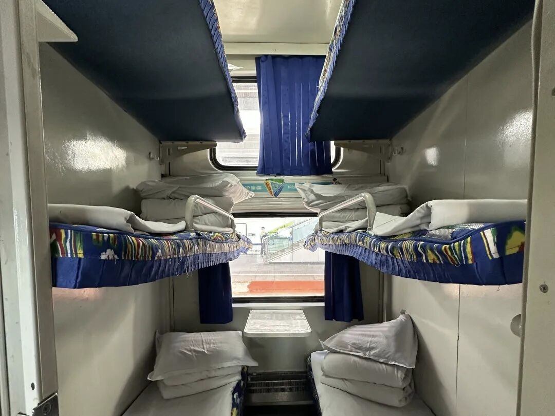 Hard-sleeper open compartment on a conventional Chinese train: six berths stacked three high on each side, no door