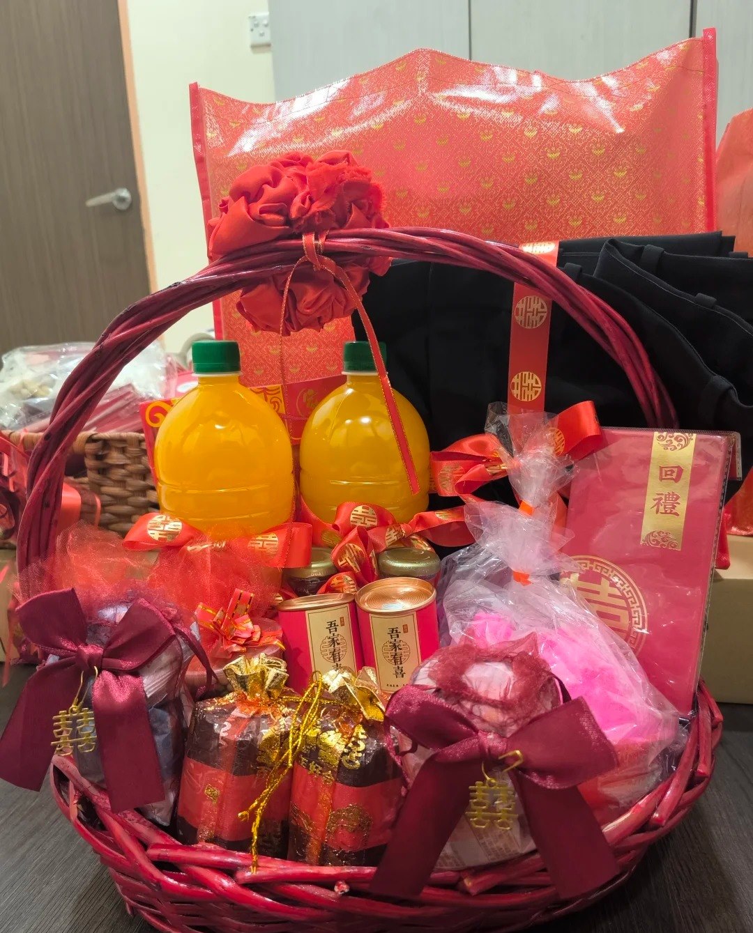 A red basket of return gifts: drinks, tea caddies marked with a happiness character, wrapped sweets, and a red box labelled 回禮