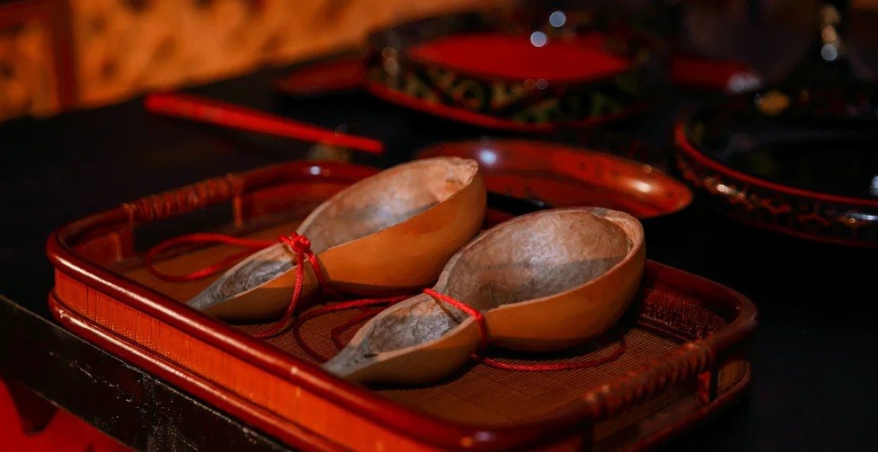 Two halves of a dried bottle gourd made into drinking ladles, joined by a red cord on a red lacquer tray
