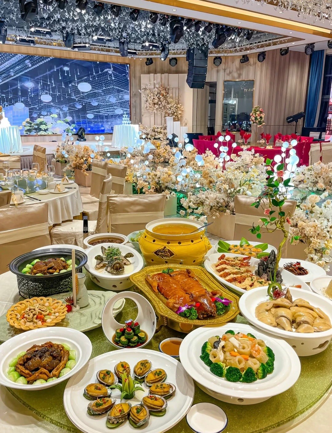 A wedding banquet table loaded with dishes including a whole roast bird, abalone, prawns and braised feet