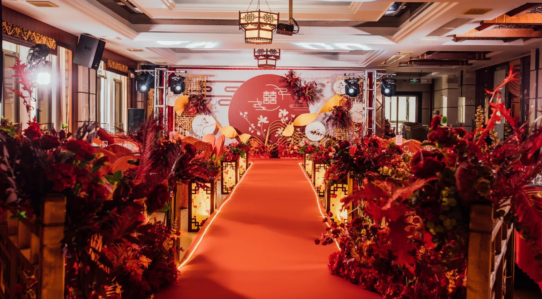 Chinese wedding ceremony aisle with a red carpet, double-happiness backdrop and lantern-lined floral arrangements