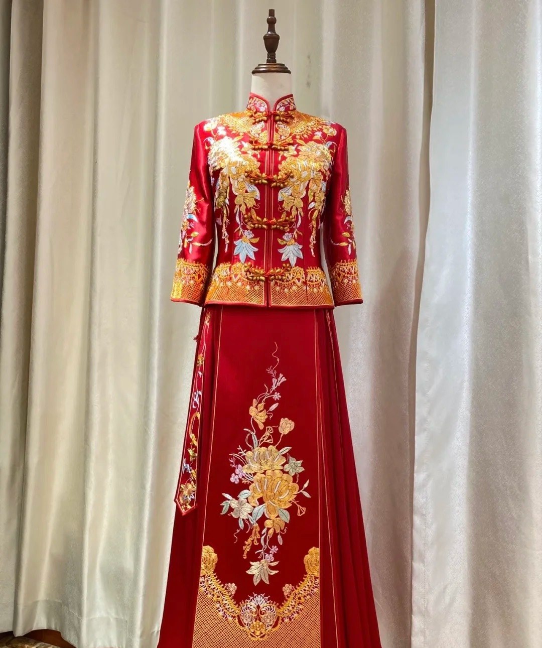 A red xiuhe wedding outfit on a dress form: a mandarin-collared jacket with a diagonal front closure over a pleated horse-face skirt