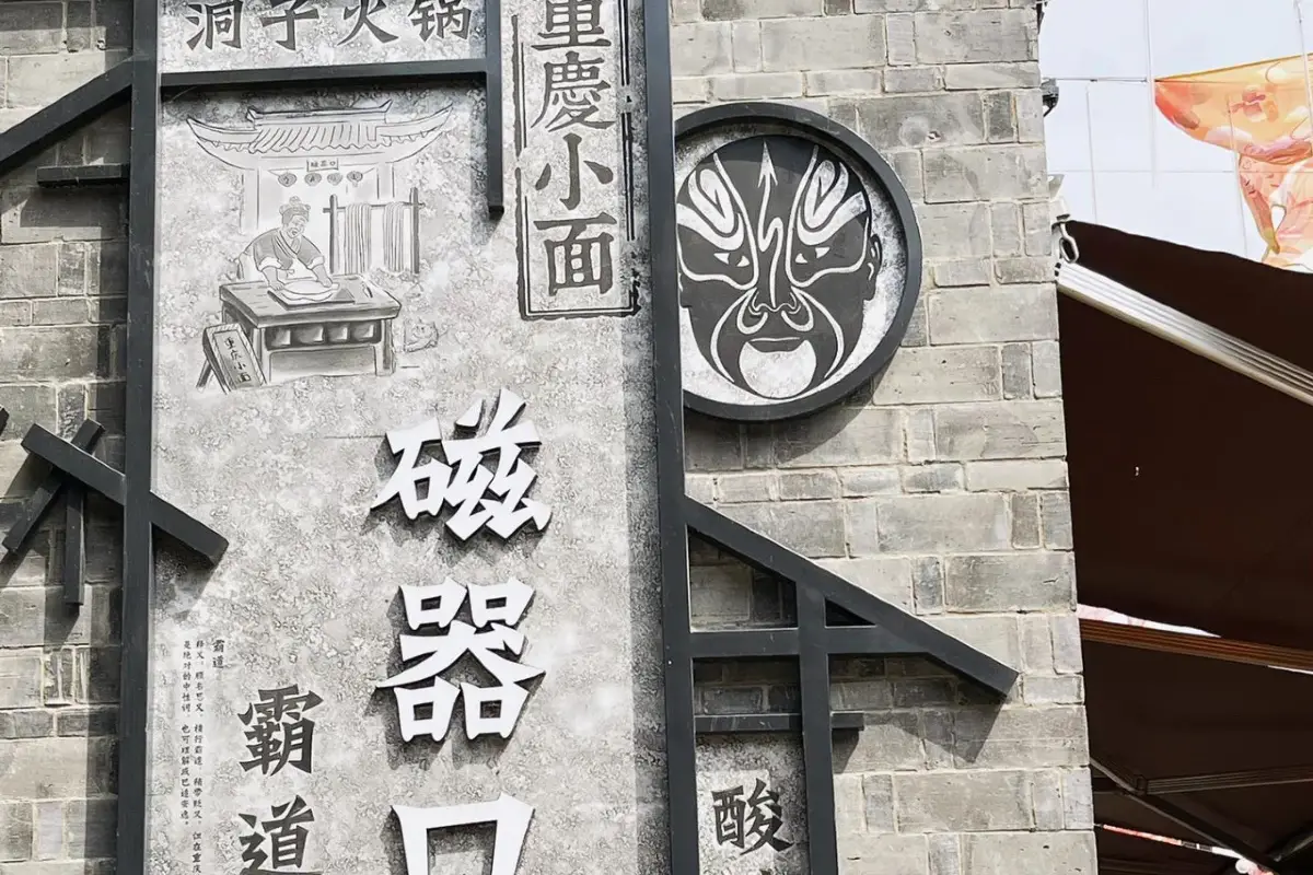 Carved stone wall reading 磁器口 with a Sichuan-opera face-mask medallion and a porcelain-maker relief, Ciqikou, Chongqing.