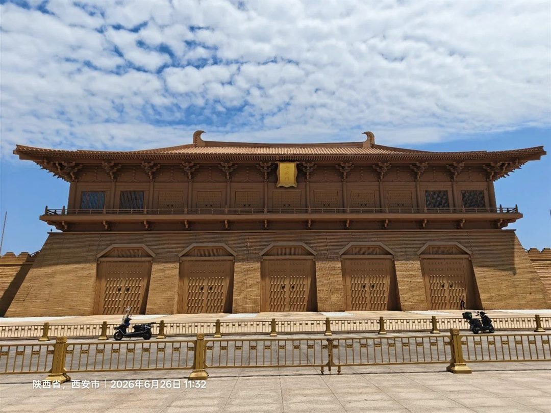 The Danfeng Gate front-on, an ochre rampart with five shut timber gateways and a gold plaque reading 丹鳳門 above them, under a blue sky.