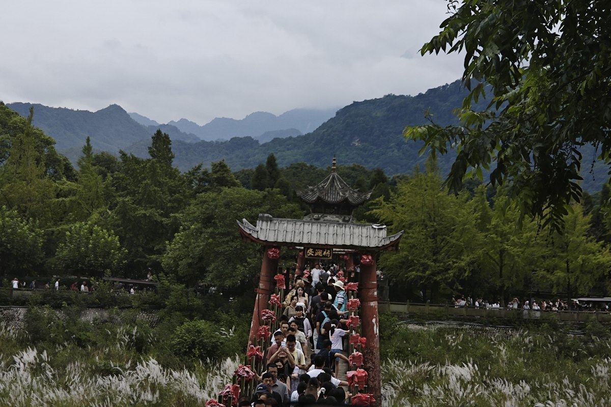 Visitors crossing the Anlan suspension bridge at Dujiangyan, with the Min River valley and mountains behind.