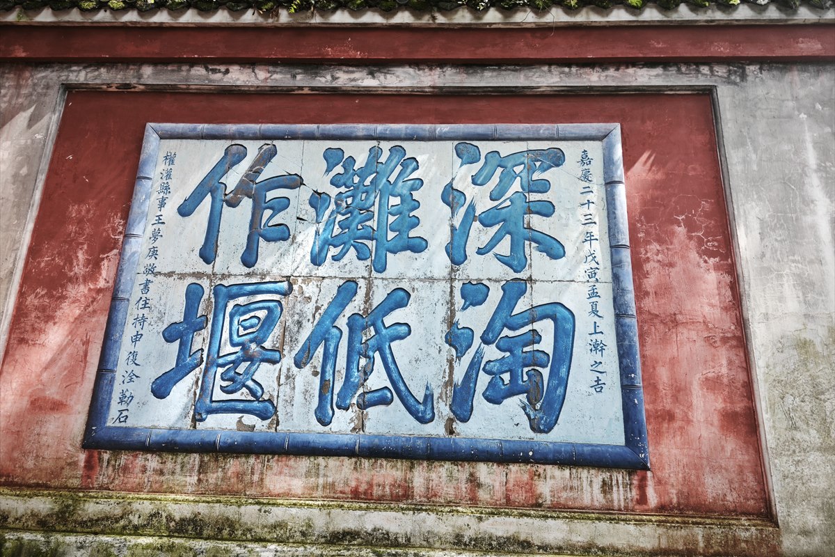 Six Chinese characters inscribed in blue on a white panel set into the red wall at Erwang Temple, Dujiangyan.