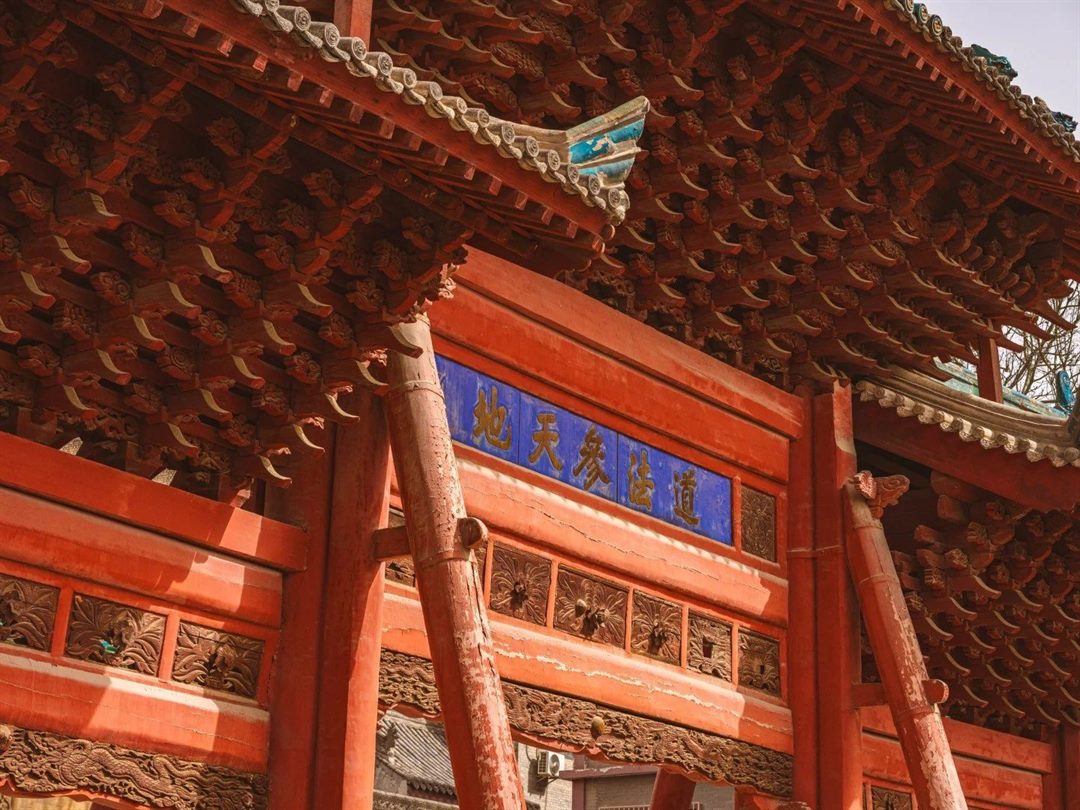 The red timber archway seen from below, dense red bracket sets filling the upper half, and a blue-and-gold horizontal plaque reading 道法参天地 set into its frame.