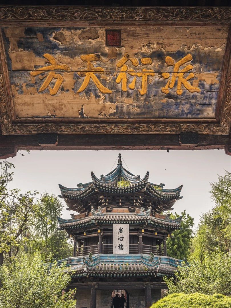The weathered 派衍天方 board with a carved dragon crown and red seal, framing the three-tier Shengxin Tower across a garden courtyard below.