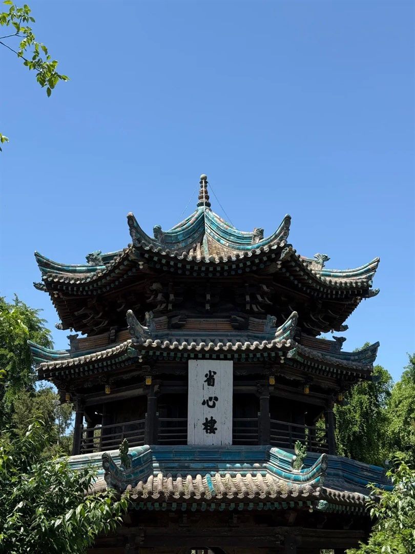 The three-storey octagonal Shengxin Tower against a clear blue sky, its turquoise-glazed ridges and eave sweeps complete, with a vertical plaque reading 省心樓.