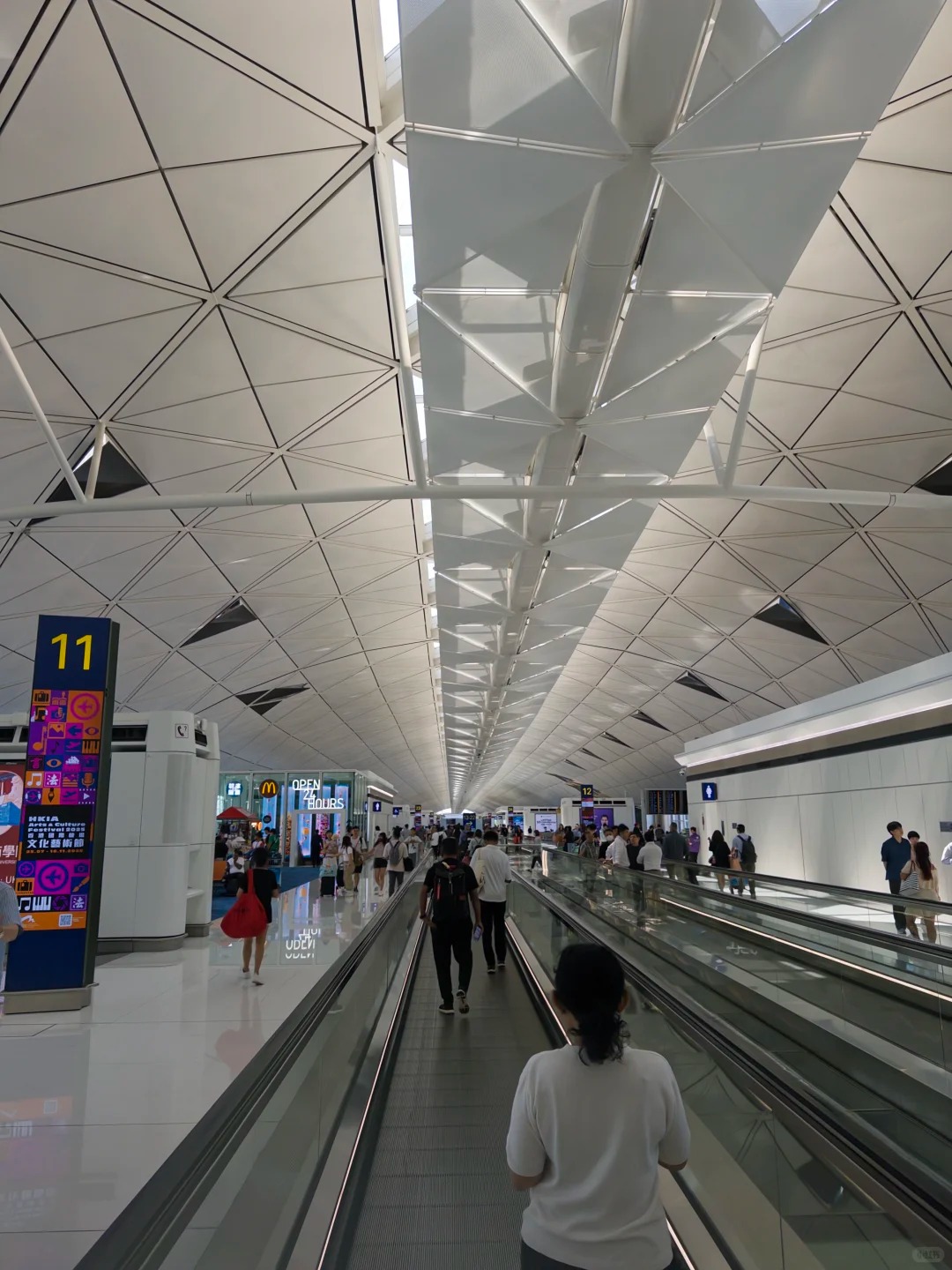 The long gate concourse at Hong Kong airport Terminal 1 with travelators under the white lattice roof, near gate 11