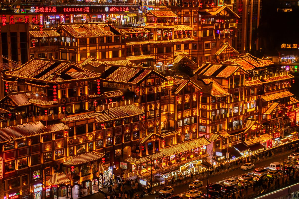 Close view of the lit Hongyadong facade at night, showing the stacked timber balconies, individual restaurant and shop signs on each level, and the street and traffic at the base.