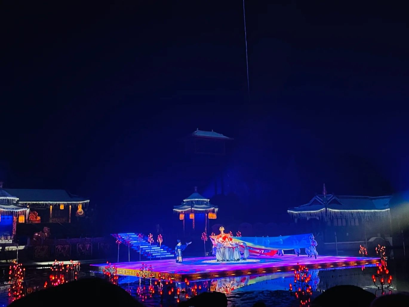 The Chang Hen Ge night performance at Huaqing Palace: a lit walkway across the water with costumed performers, lantern-hung pavilions on both sides, and the dark mass of Mount Li behind.