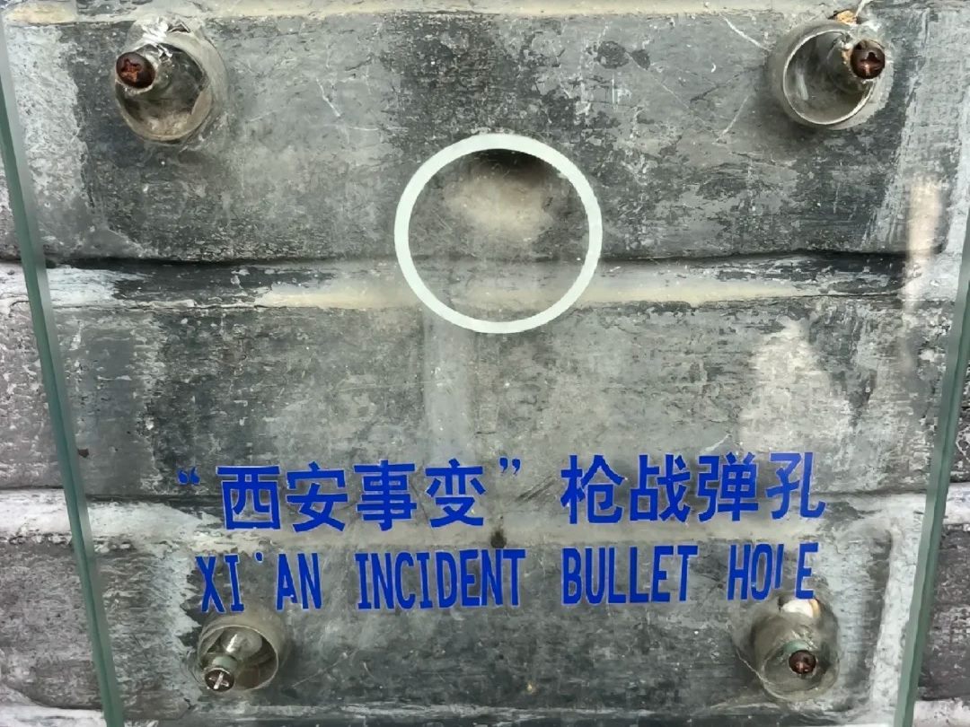 A glass plate bolted over stonework at Huaqing Palace, a white ring marking a bullet hole, engraved in Chinese and English: Xi'an Incident bullet hole.
