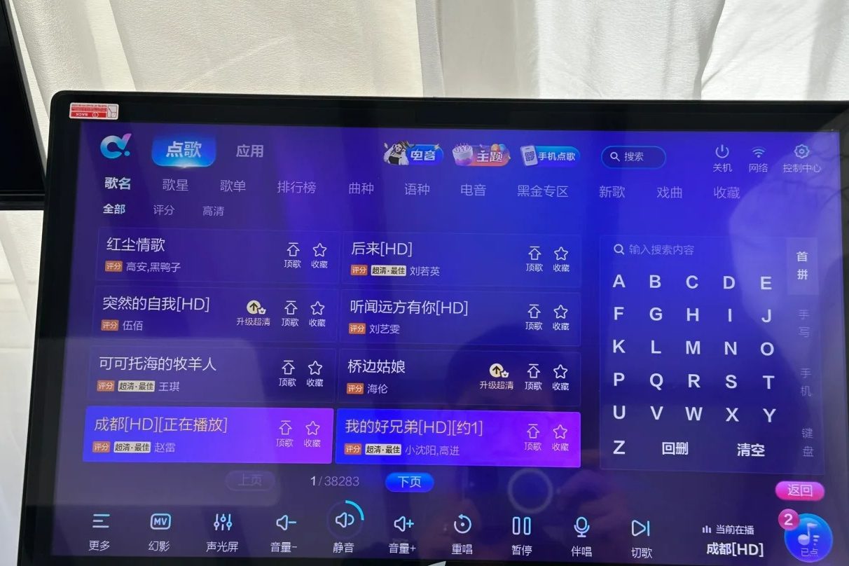 A KTV song-request touchscreen showing a Chinese-language interface: search box, category tabs for song name, artist, playlists and rankings, and a grid of song titles.