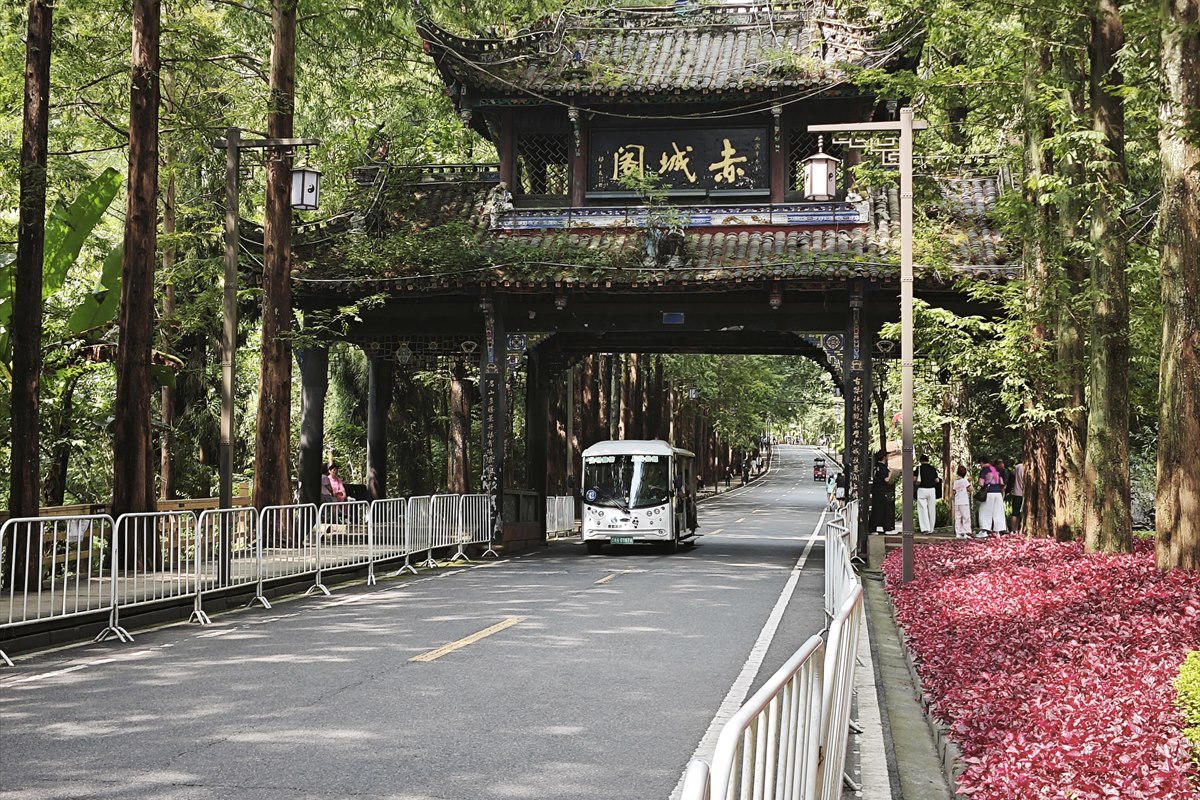 A tiered gate-pavilion spanning the approach road to Mount Qingcheng, with an electric shuttle cart passing beneath it.