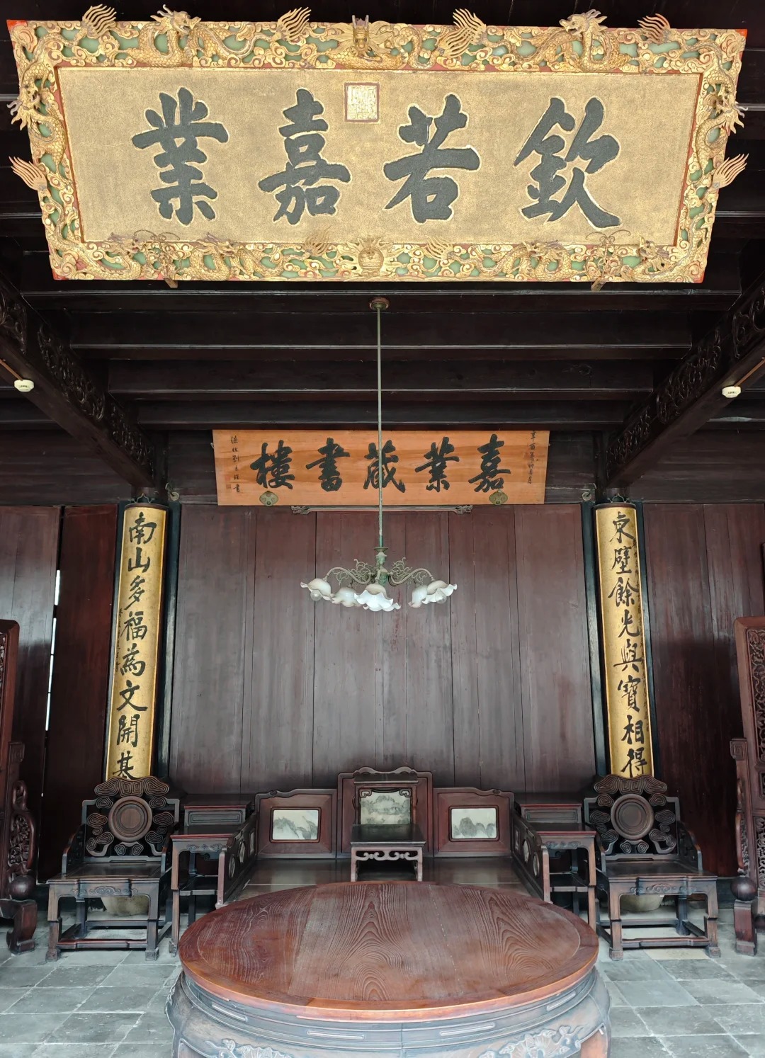 The main hall of the Jiaye Library in Nanxun: a gilded imperial plaque reading Qin Ruo Jia Ye in a dragon-carved frame hangs above a smaller board reading Jiaye Cangshulou, over dark rosewood chairs and a round table.
