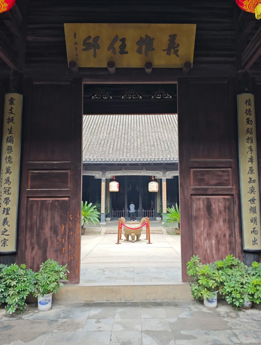 Looking through the open doors of the Liu family temple in Nanxun: a gilded board reading Yi Tui Ren Xu hangs over the entrance between two vertical inscribed panels, with a bronze censer and a tiled hall beyond in the courtyard.