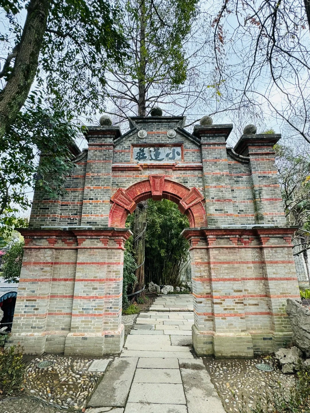 The gateway to the Xiaolianzhuang garden in Nanxun: a grey brick screen wall banded with red brick, pierced by a Western-style round arch, with a stone plaque reading Xiaolianzhuang set above it and bamboo visible through the opening.