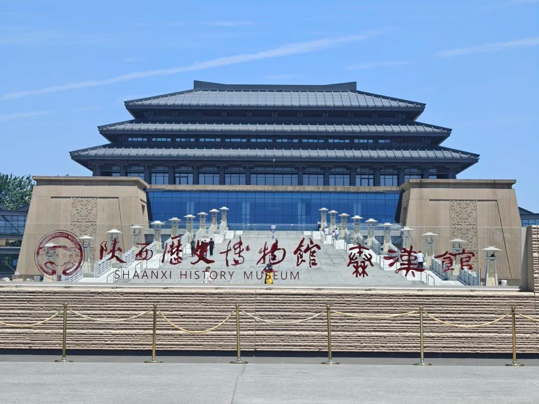 A large modern museum building with a stepped dark-glass roof on a stone podium, with a sign reading Shaanxi History Museum Qin-Han Museum.