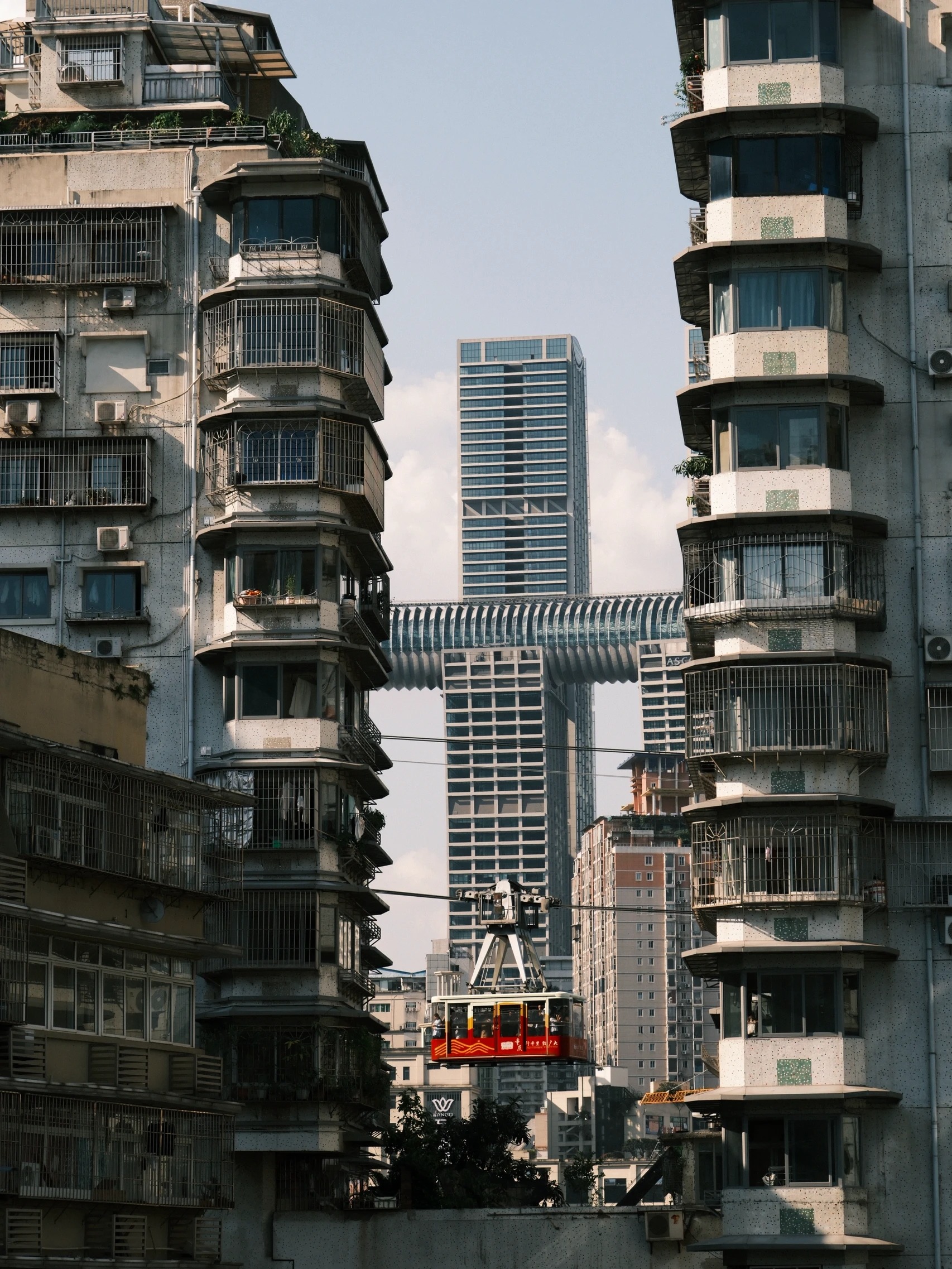 A red and cream cable car cabin crossing between two old residential towers, with the horizontal crystal skybridge of Raffles City visible in the gap behind.