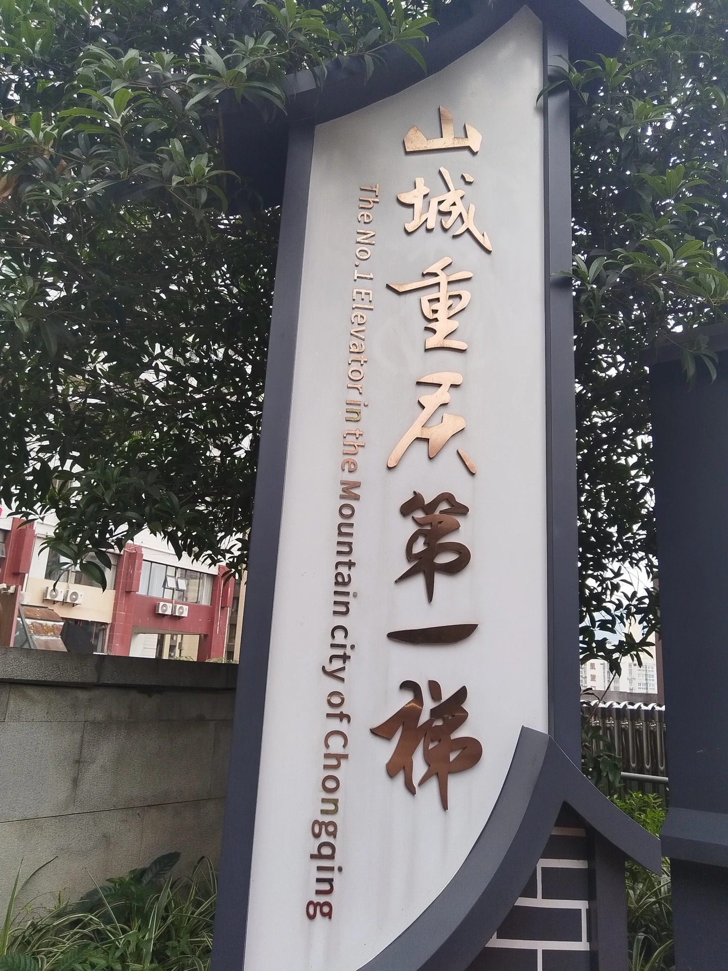 A bilingual signboard reading 山城重庆第一梯 in gold characters with the English line The No.1 Elevator in the Mountain city of Chongqing running vertically beside it.
