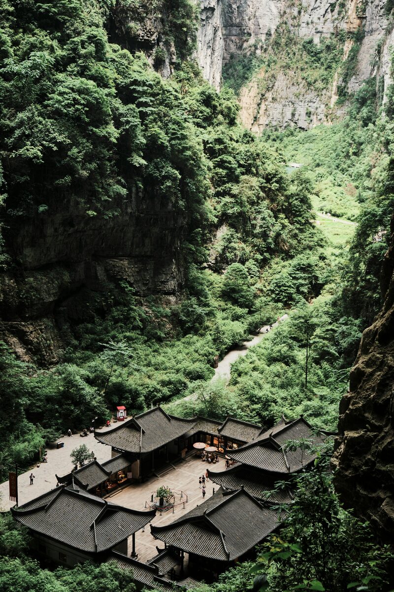 The Tianfu Inn courtyard rooftops set deep in the Wulong karst slot canyon, with the stream path winding through the forested gorge.