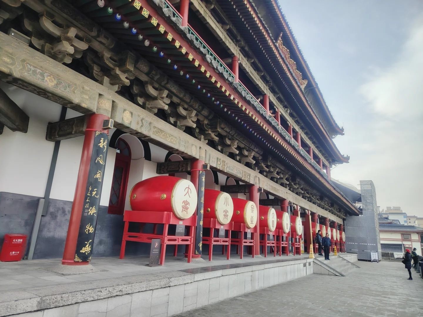 The Drum Tower's lower gallery at eye level, a row of large red drums with gold-lettered heads receding along the terrace beneath painted eaves.