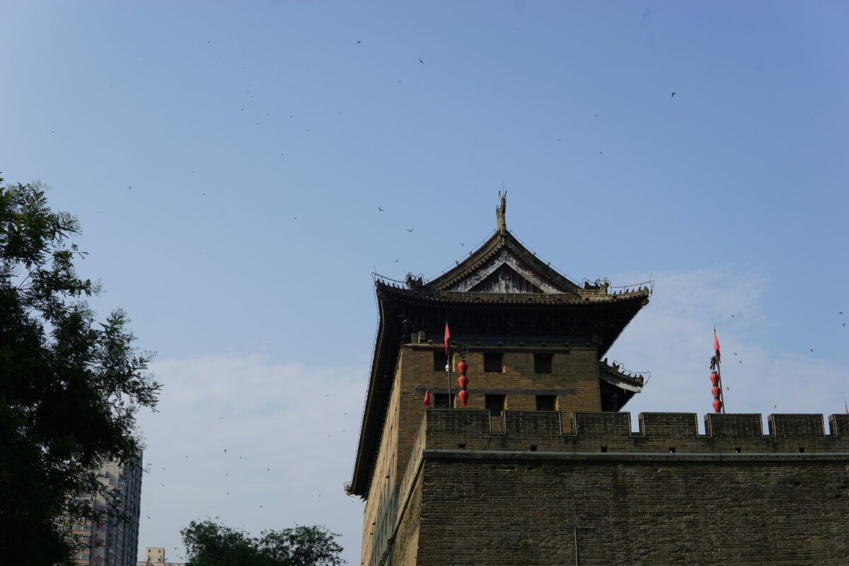 Xi'an City Wall corner gate tower with upturned eaves and red lanterns against a blue sky, swifts circling overhead.