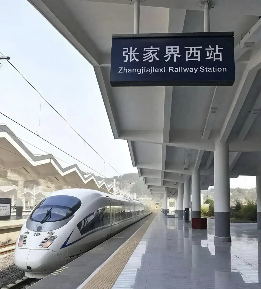A white CRH high-speed train at the platform of Zhangjiajie West, beneath the bilingual Zhangjiajiexi Railway Station platform sign.